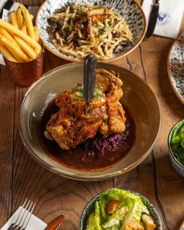 plate with crispy roasted pork knuckle held with knife and rich gravy